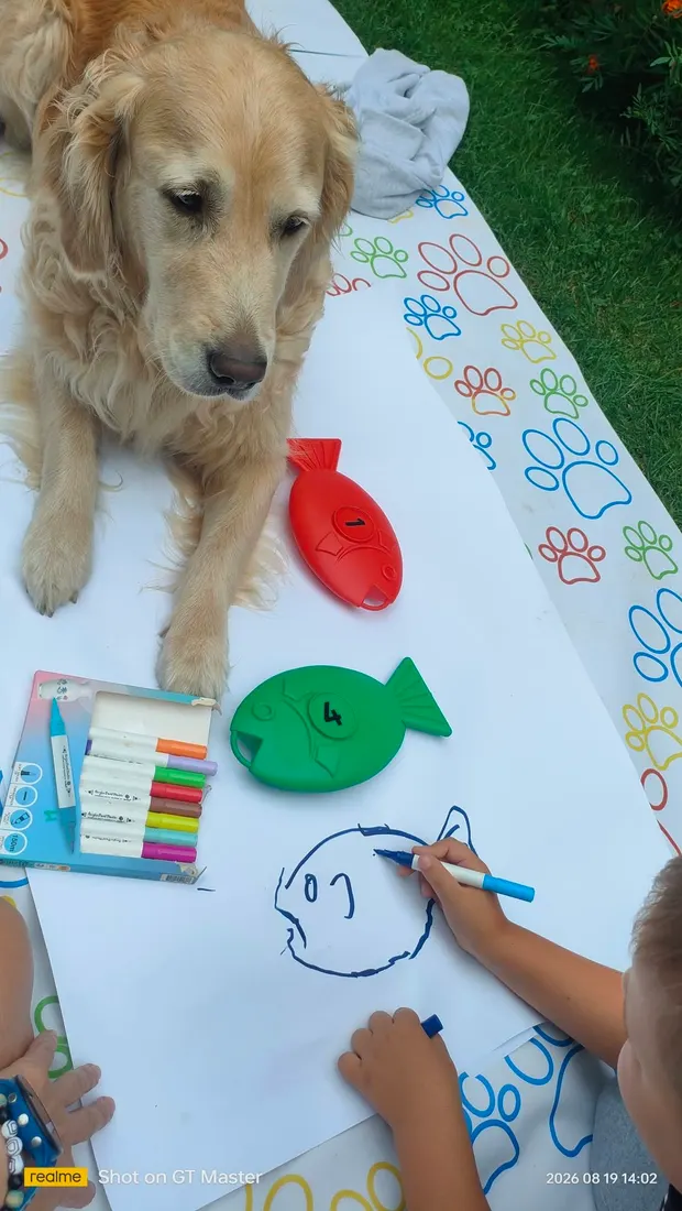 Dziecko rysuje kredkami na dużej kartce, Carmen leży przy niej na macie